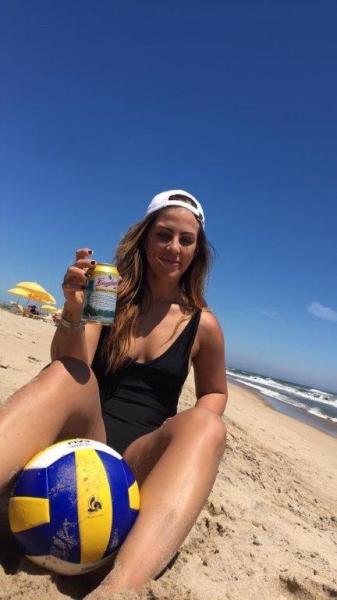 A girl on vacation relaxes on a Hamptons beach with a beer and a volleyball. 