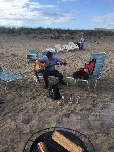 the rabbi tunes his guitar for our havdalah ceremony on the beach during our weekend for young jewish professionals from nyc