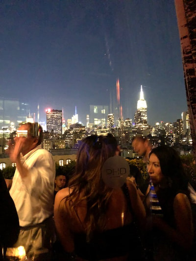 The crowd enjoying themselves at the best rooftop party in NYC with the Manhattan skyline in the background at night. 